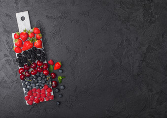 Fresh organic summer berries mix on white marble board on dark kitchen table background. Raspberries, strawberries, blueberries, blackberries and cherries. Space for text