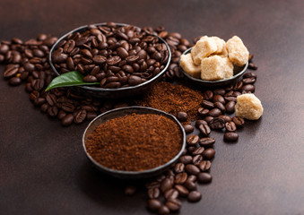 Fresh raw organic coffee beans with ground powder and cane sugar cubes with coffee trea leaf on brown background.