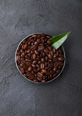Fresh raw organic coffee beans in steel bowl with coffee trea leaf on black background.