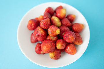 summer berry. juicy red strawberries on white plate on blue background. Delicious breakfast snack. Vegetarian food. useful vitamins. isolated.