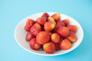 summer berry. juicy red strawberries on white plate on blue background. Delicious breakfast snack. Vegetarian food. useful vitamins. isolated.