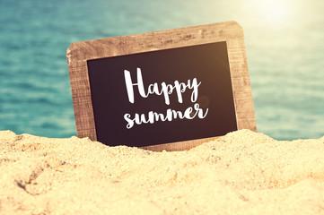 Happy summer written on a vintage chalkboard in the sand of a beach