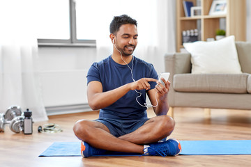 sport, technology and healthy lifestyle concept - smiling indian man in earphones listening to...
