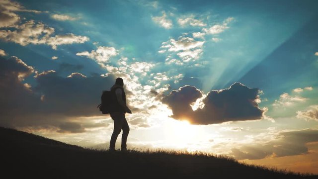 The Silhouette of two man on the top of mountain with Backpacks and other Gear expressing Energy and Happiness. Two tourist young men on rocky cliff and enjoying view. Travel concept.