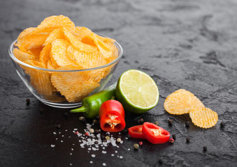 Glass bowl plate with potato crisps chips with paprika flavour on black stone table background. Red...