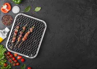 Grilled pork kebab with paprika on disposable coal bbq grill with fresh vegetables on...