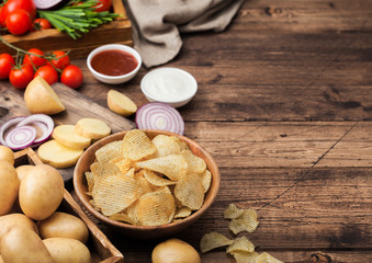 Fresh organic homemade potato crisps chips in wooden bowl with sour cream and red onions and spices on wooden table background. Fresh yellow potatoes with ketchup