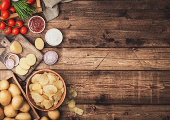 Fototapeta na wymiar Fresh organic homemade potato crisps chips in wooden bowl with sour cream and red onions and spices on wooden table background. Top view.Fresh yellow potatoes with ketchup