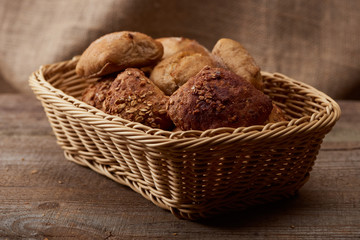 delicious bread and buns in wicker box on wooden table