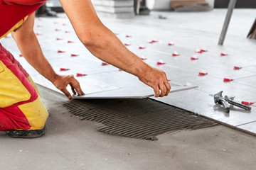 Ceramic Tiles. Tiler placing ceramic wall tile in position over adhesive with lash tile leveling...