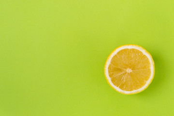 Round slice of yellow lemon, on a green background. There is a place of text.