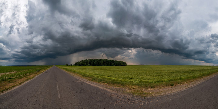 hdr panorama on asphalt road among fields in evening with awesome black clouds before storm