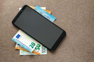 New black modern digital cellphone on money euro banknotes on copy space texture background. Modern technology, communication and online trade using gadget concept.