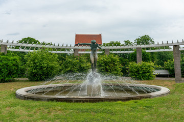 Fountain of a woman on Zeltinger Platz in Berlin Frohnau with pergola and church in the background