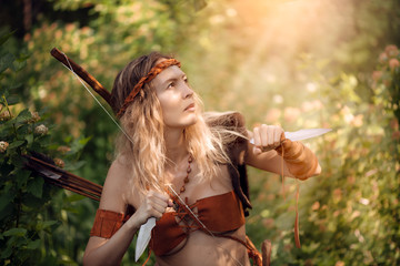 Beautiful girl archer with long blond hair with bow and arrowson a back holding two steel knifes...