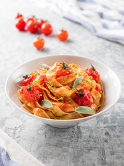 Italian pasta tagliatelle with tomatoes and green on a light background.