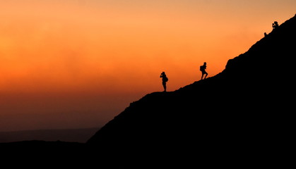 Silhouette of people walking on a mountain in front of a sunrise