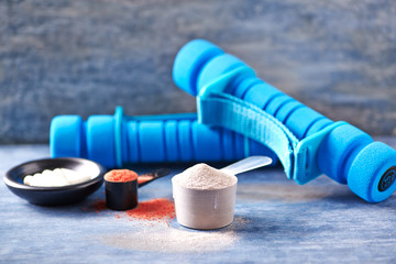 Scoop of Whey Protein, Creatine Powder, Taurine capsules and blue Dumbbells in background. Sport nutrition. Rustic wooden background. Close up. Copy space