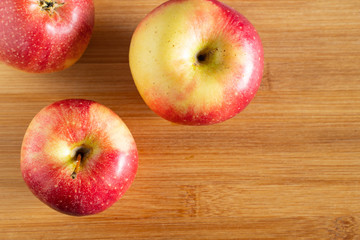 three beautiful red-yellow apples lie on a wooden triangle background in the corner