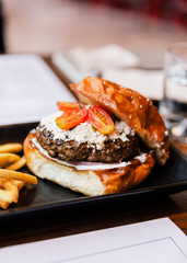 Close up Cheeseburger with grilled beef, feta cheese and sliced tomato served with fries in black plate.