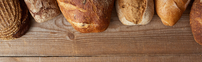 top view of fresh homemade loaves of bread on wooden table, panoramic shot