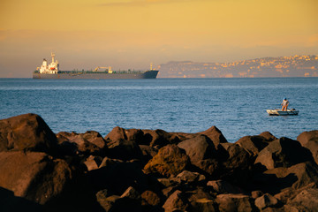 Unrecognizable man sailing on a boat with oars in the sea, a fisherman in a boat over a huge liner