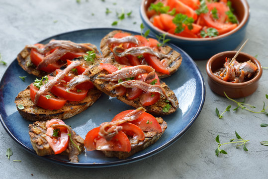 Gegrillte kleine Brotscheiben mit Oliven&ouml;l und K&auml;utern, frischen Tomaten und Chili-Sardellen-Filets &ndash;Spanish tapas: Grilled slices of bread with olive oil, herbs, tomatoes and spicy anchovy fillets