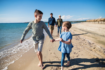 Young family with two small children walking outdoors on beach.