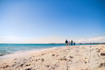 Rear view of young family with two small children walking outdoors on beach.