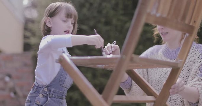 Mother painting chair with daughter in garden