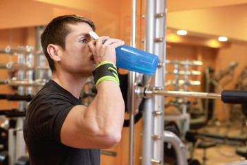 Muscular man drink water from blue bottle in the gym .