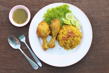 Muslim yellow rice with chicken in a white plate on a wooden floor