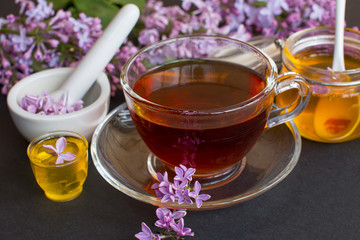 a jar of fragrant flower honey. Honey saved and lilac flowers. Cup of black tea.
