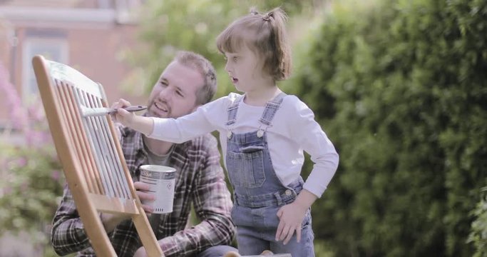 Father painting chair with daughter in garden