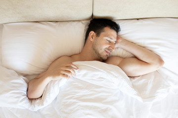 Obraz na płótnie Canvas Handsome young man sleeping in white bedding.