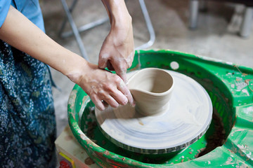 Young woman novice student in the first lesson in pottery tries to make a product from white clay on a potter's wheel. reportage. small sauce pan. making a spout
