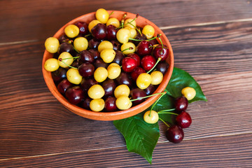Yellow and red sweet cherry in a clay plate on a wooden background. Freshly picked sweet cherry