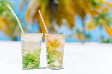 Two cold tasty mohito cocktails on the white sandy beach in palm grove
