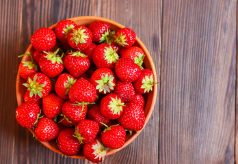 Red tasty strawberries in a clay plate on a wooden background. Freshly picked strawberries