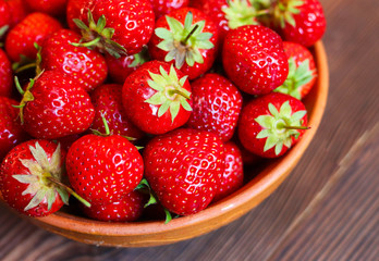 Red tasty strawberries in a clay plate on a wooden background. Freshly picked strawberries