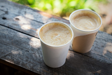 Two paper cups of coffee on a wooden terrace outdoors