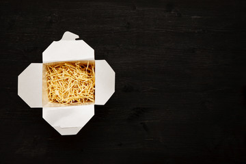 Dry noodles in paper box on a black table, top view, text space