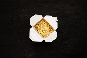 Dry noodles in paper box on a black table, top view