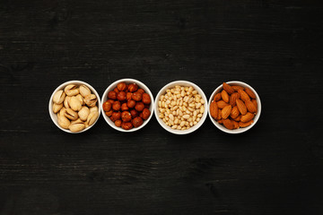 Different nuts in ceramic bowls on a black wooden table, top viev