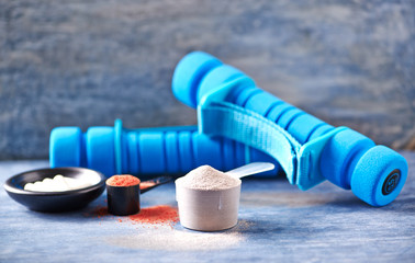 Scoop of Whey Protein, Creatine Powder, Taurine capsules and blue Dumbbells in background. Sport nutrition. Rustic wooden background. Close up. Copy space