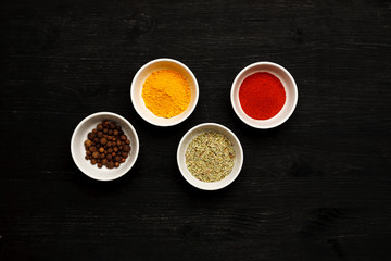 Different spices in ceramic bowls on a black wooden table, top view