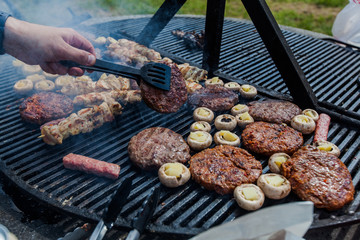Preparing grilled meat on barbecue at picnic