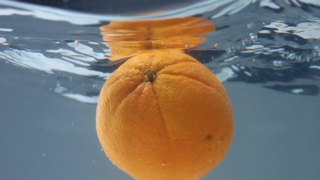 an orange falling in water, underwater view. With water surface reflecting an orange