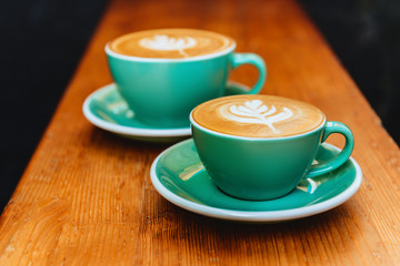 Two cups of cappuccino with latte art on wooden background.