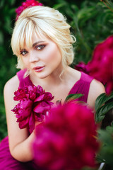 Naklejka premium Outdoor close up portrait of beautiful young woman with long blonde hair, makeup, posing in the blooming garden. Female spring fashion concept